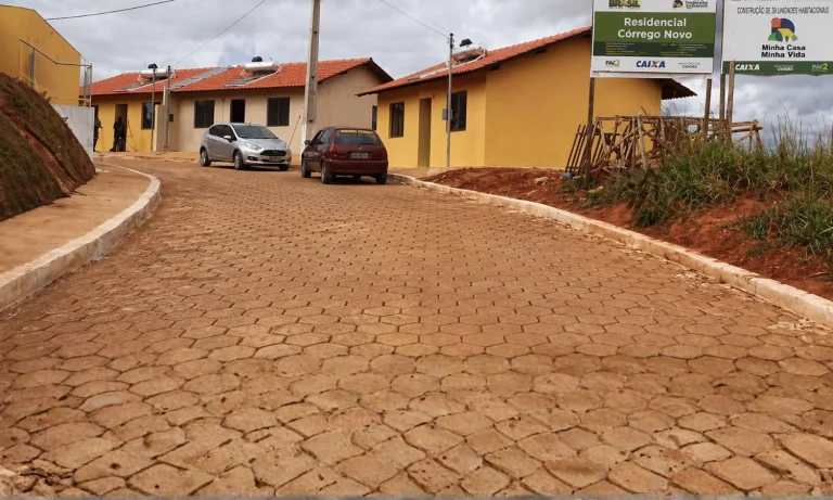Rua pavimentada com blocos intertravados em conjunto habitacional com casas térreas amarelas e carros estacionados.