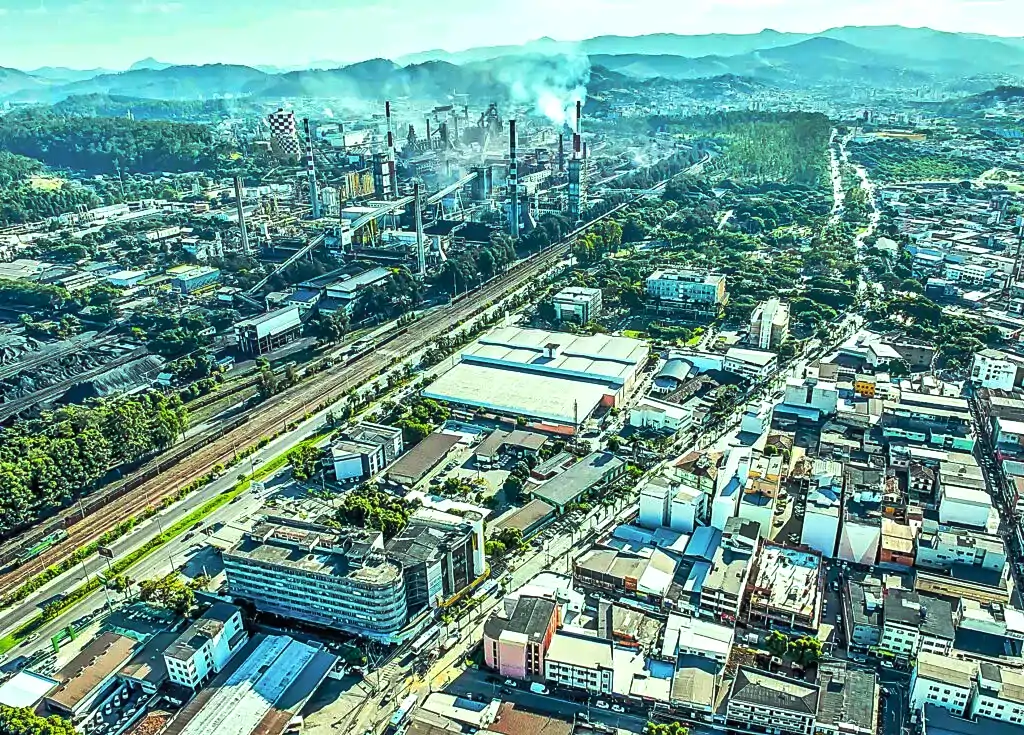 Vista aérea do Vale do Aço, em Minas Gerais, mostrando área urbana, vias, linha férrea e complexo industrial ao fundo.
