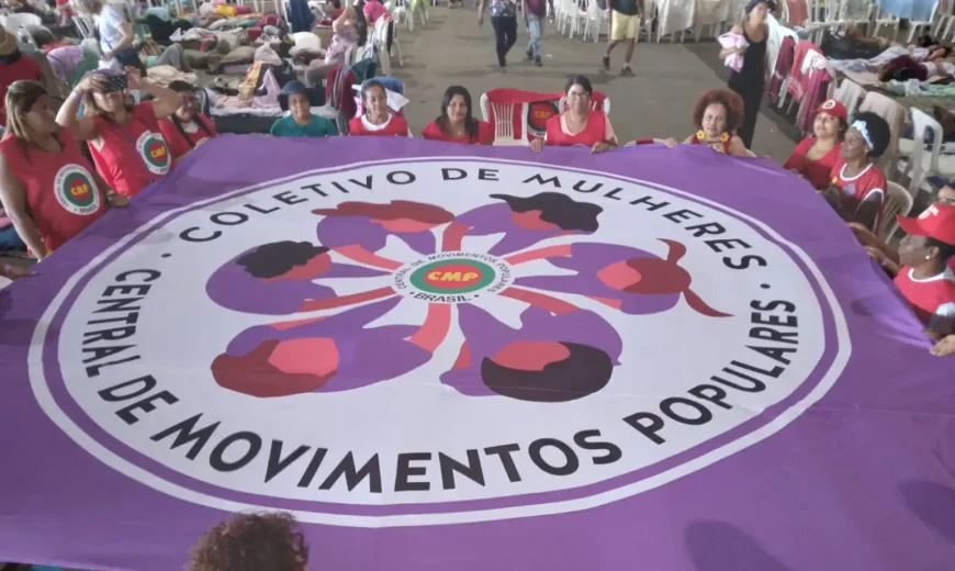 Mulheres seguram grande bandeira roxa do Coletivo de Mulheres da Central de Movimentos Populares durante atividade coletiva em espaço amplo.