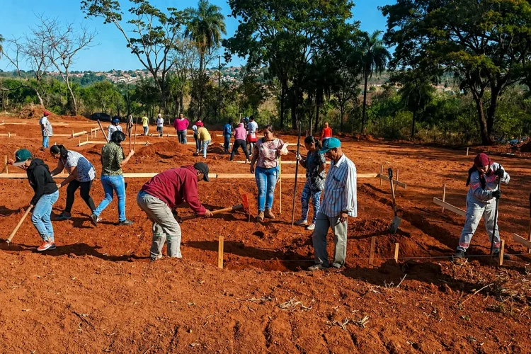 Grupo de pessoas trabalhando em mutirão na preparação de terreno para construção de moradias em área aberta.
