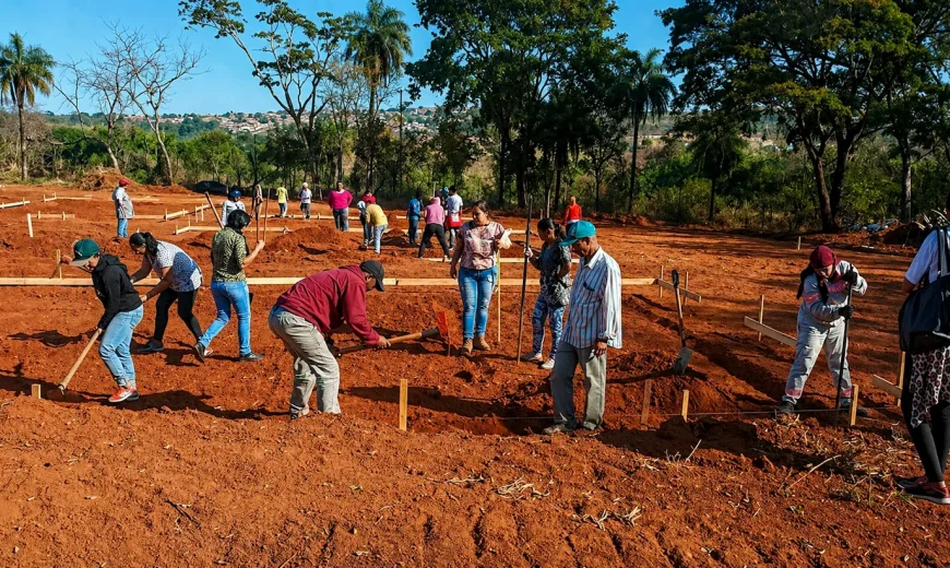 Grupo de pessoas trabalhando em mutirão na preparação de terreno para construção de moradias em área aberta.