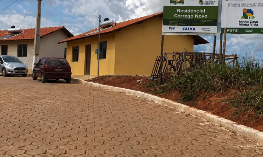 Conjunto habitacional com casas térreas, rua pavimentada e placa do programa Minha Casa Minha Vida no Residencial Córrego Novo
